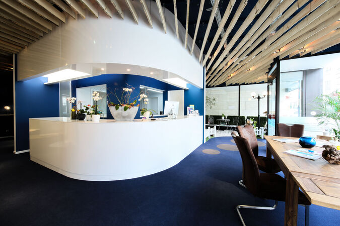 Modernes Empfangsbereich einer Praxis mit weißem Tresen, Pflanzen und stilvollem Design.