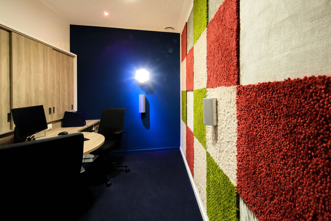 Modernes Büro mit Schreibtischen, blauer Wand und bunter Akustik-Paneel-Wand.