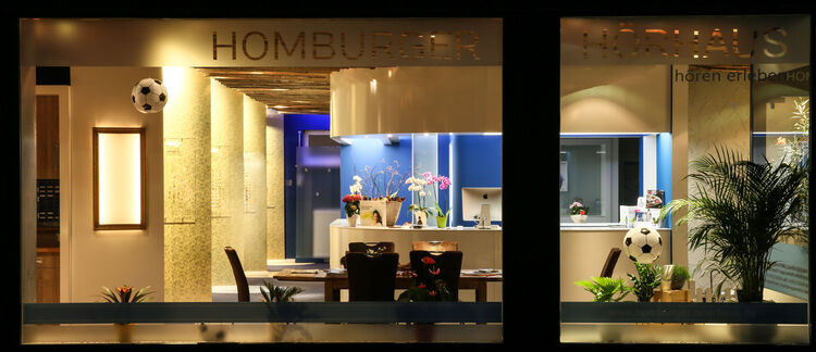 Modernes Hörakustik-Fachgeschäft mit Pflanzen, Computer und Fußball-Dekoration im Schaufenster.